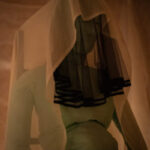 Green fabric sculpture sitting on a chair, wearing white and black veils.
