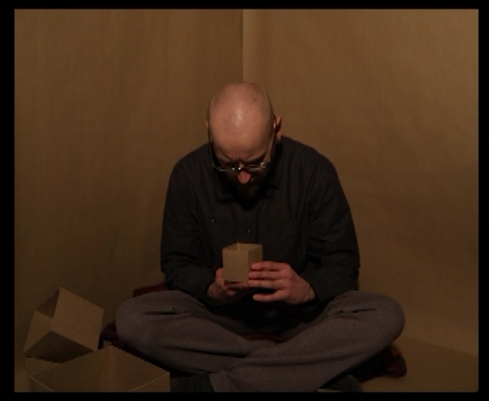 A human sitting in a box is peering into a box.