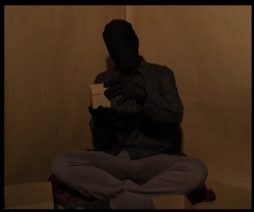 A darkened figure sits in a box with a box in their hands.